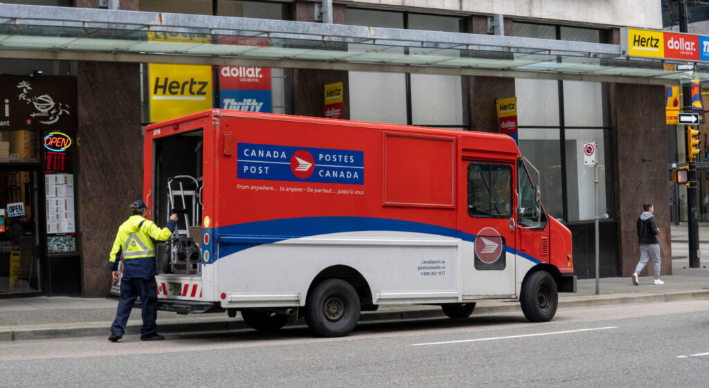 Canada Post van with a worker pulling a dolly from the open back door.